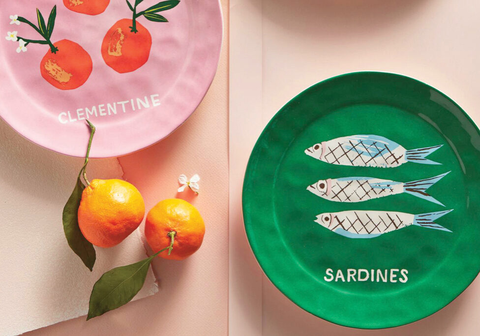 Two dinner plates, a green plate with sardines painted on it and a pink plate with clementines painted on